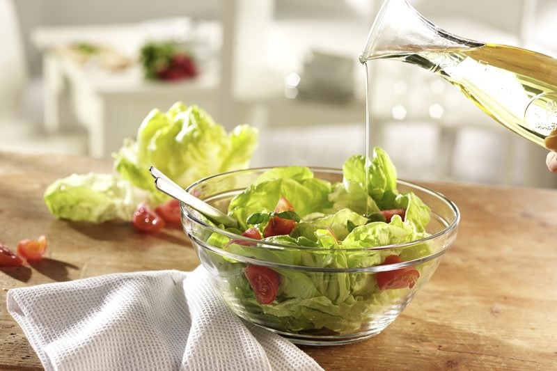 pouring salad dressing over a green salad