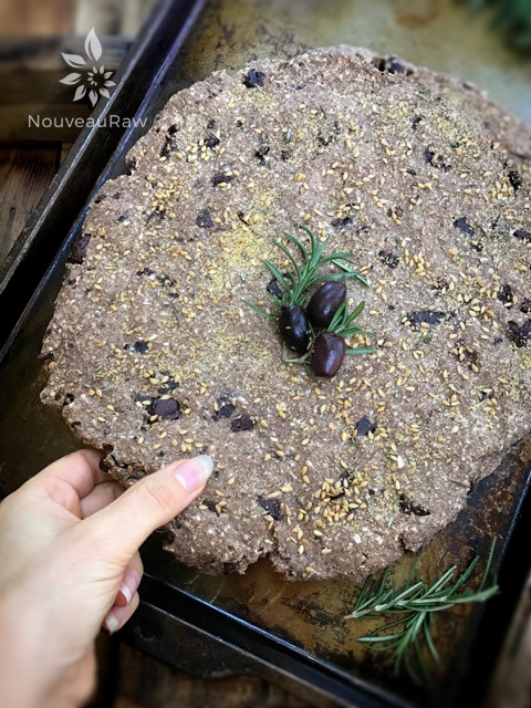 lifting up a piece of raw vegan gluten-free Kalamata Olive and Rosemary Focaccia