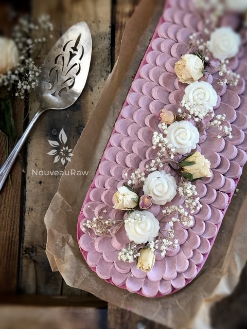 a close up raw vegan Prickly Pear Cheesecake decorated with coconut roses and serving utensil