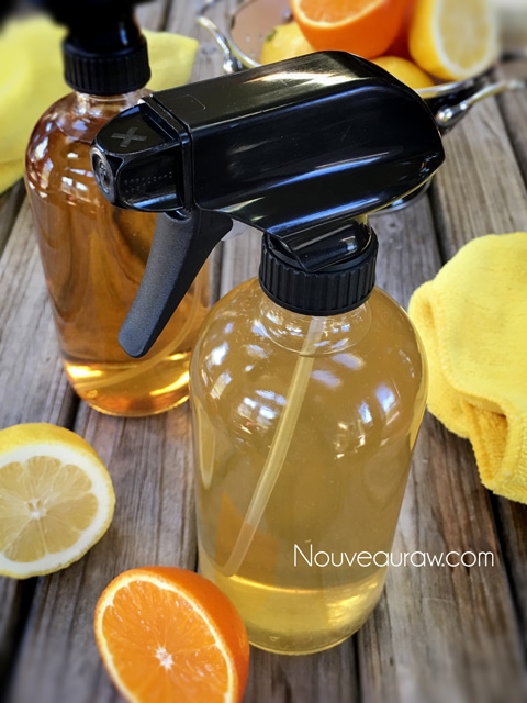 a close up of Citrus Household Cleaner in glass spray bottles and displayed on a wood table with citrus fruit