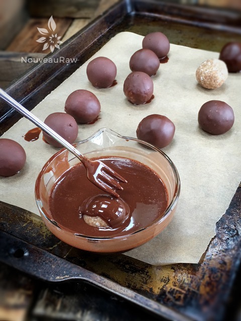 dipping the the inside of a raw vegan Chocolate Covered Salted Caramel Macaroon in chocolate