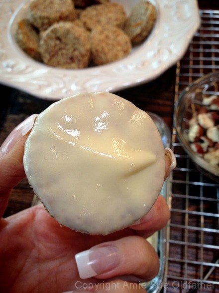 close up of dipping the Cardamon Orange Hazelnut Biscuit into a Orange Butter Glaze 