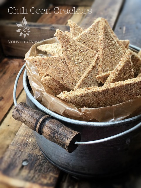 raw vegan Chili Corn Crackers displayed in an old bucket on a piece of barnwood