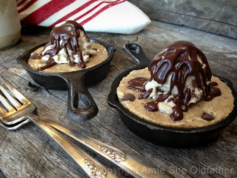 drizzling chocolate sauce over the raw vegan gluten-free Chocolate Chip Skillet Cookie served with Ice Cream on barn wood