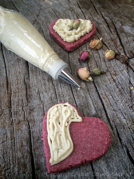 adding frosting on raw vegan Rosewater Sugar Cookies and adding dried flowers