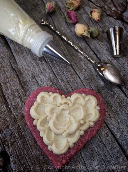 demonstrating piping frosting on raw vegan Rosewater Sugar Cookies and adding dried flowers