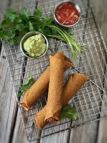 raw vegan “Refried Bean" Taquitos displayed on a wire rack with guacamole and salsa