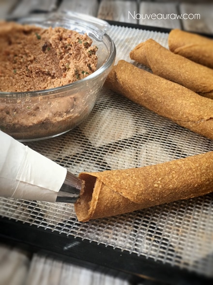 a close up of piping the refried beans in the “Refried Bean" Taquitos shell